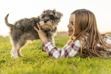 Smiling girl lying on a meadow playing with dog - ERRF00686