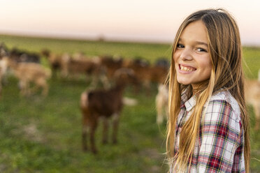 Porträt eines grinsenden Mädchens auf einer Weide mit einer Ziegenherde im Hintergrund - ERRF00697