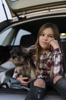 Portrait of girl sitting in opened boot with her dog pouting mouth - ERRF00713