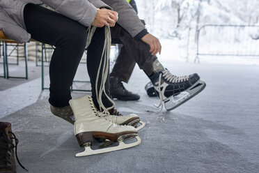 Couple sitting on bench at the ice rink, putting on ice skates - ZEDF01828