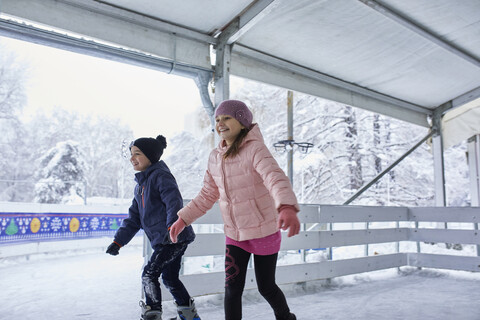 Bruder und Schwester beim Schlittschuhlaufen auf der Eislaufbahn, lizenzfreies Stockfoto