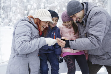 Familie mit zwei Kindern auf der Eisbahn, die sich Selfies auf ihrem Smartphone ansehen - ZEDF01833