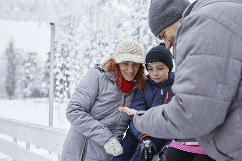 Familie mit zwei Kindern auf der Eisbahn, die sich Selfies auf ihrem Smartphone ansehen - ZEDF01834