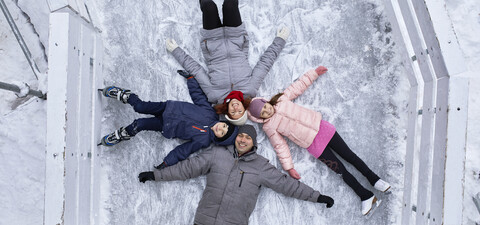 Familie mit zwei Kindern auf der Eislaufbahn, auf dem Eis liegend, lizenzfreies Stockfoto