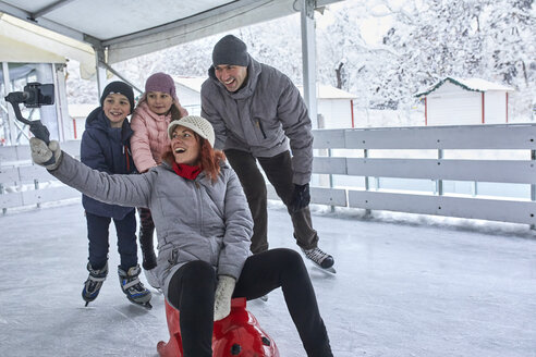 Familie mit zwei Kindern auf der Eisbahn, die Selfies mit ihrem Smartphone machen - ZEDF01856