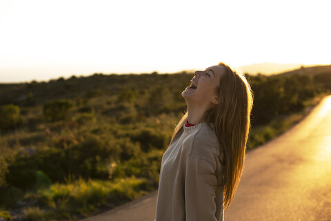 Lachende junge Frau auf Landstraße bei Sonnenuntergang, lizenzfreies Stockfoto