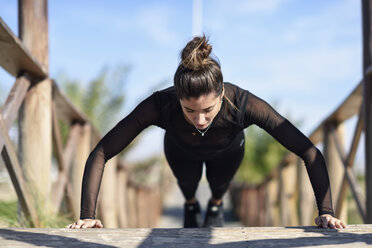 Sportive woman doing push-ups on wooden bridge - JSMF00757