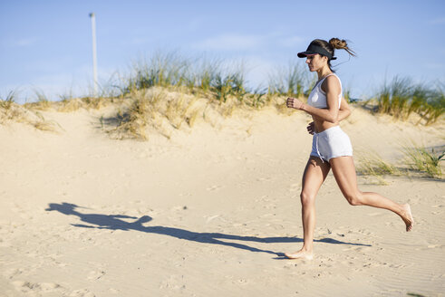 Sportliche Frau, die am Strand entlang der Sanddünen läuft - JSMF00768