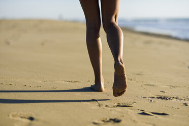 Close-up of woman's legs walking in sand on the beach - JSMF00781