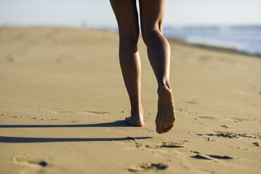 Nahaufnahme der Beine einer Frau, die am Strand im Sand läuft - JSMF00781