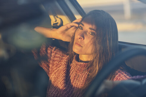 Porträt einer ernsten Frau, die bei Sonnenuntergang im Auto sitzt - JSMF00797