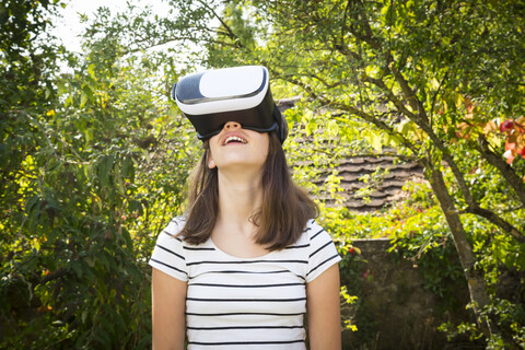 Erstauntes Mädchen mit Virtual-Reality-Brille im Garten, lizenzfreies Stockfoto