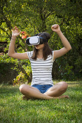 Mädchen sitzt auf einer Wiese im Garten und benutzt eine Virtual-Reality-Brille - LVF07715