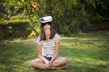 Mädchen sitzt auf einer Wiese im Garten und benutzt eine Virtual-Reality-Brille - LVF07716