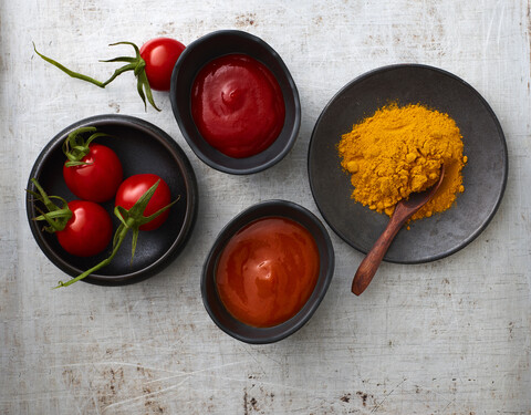 Tomaten, Currypulver, Chili-Ketchup und Tomatenketchup in Schalen, lizenzfreies Stockfoto