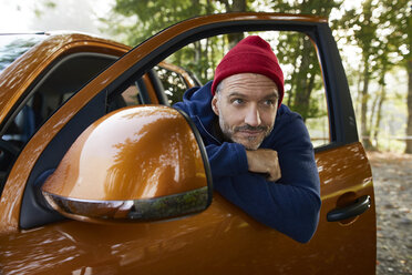 Porträt eines bärtigen reifen Mannes mit roter Mütze, der sich aus dem Fenster einer offenen Autotür lehnt - PNEF01186
