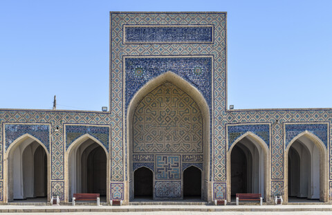 Madrasa-Fassade mit hohem Bogen und blauen glasierten Keramikfliesen, verzierten Wänden und einem Säulengang in Buchara., lizenzfreies Stockfoto