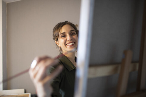 Porträt einer lächelnden jungen Frau, die in ihrem Atelier malt - GRSF00075