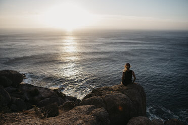 Südafrika, Westkap, Frau sitzt auf einem Felsen und beobachtet den Sonnenuntergang, gesehen vom Chapman's Peak Drive - LHPF00412