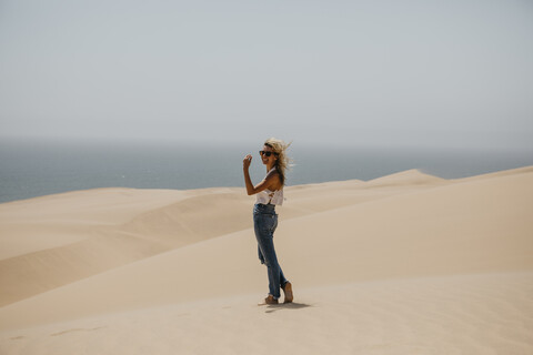 Namibia, Walvis Bay, Namib-Naukluft-Nationalpark, Sandwich Harbour, glückliche Frau in Dünenlandschaft, lizenzfreies Stockfoto