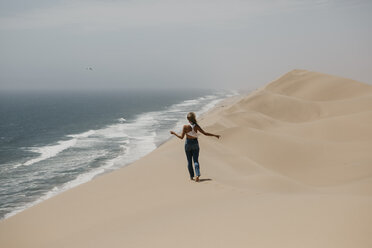 Namibia, Walvis Bay, Namib-Naukluft-Nationalpark, Sandwich Harbour, Frau spaziert in Dünenlandschaft am Meer - LHPF00436