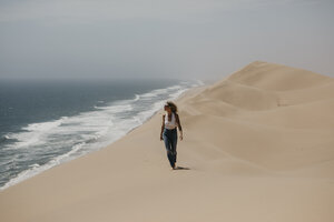 Namibia, Walvis Bay, Namib-Naukluft-Nationalpark, Sandwich Harbour, Frau spaziert in Dünenlandschaft am Meer - LHPF00437