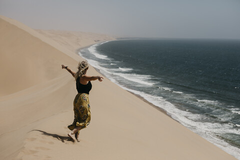 Namibia, Walvis Bay, Namib-Naukluft-Nationalpark, Sandwich Harbour, Frau spaziert in Dünenlandschaft am Meer, lizenzfreies Stockfoto