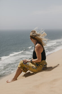 Namibia, Walvis Bay, Namib-Naukluft-Nationalpark, Sandwich Harbour, Frau sitzt in Dünenlandschaft am Meer - LHPF00440