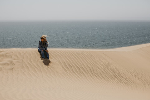 Namibia, Walvis Bay, Namib-Naukluft National Park, Sandwich Harbour, woman sitting in dune landscape at the sea stock photo