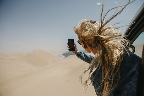 Namibia, Walvis Bay, Namib-Naukluft-Nationalpark, Sandwich Harbour, Frau lehnt sich aus dem Autofenster und macht ein Foto mit dem Handy - LHPF00442