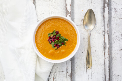 Schale mit Karotten-Ingwer-Kokos-Suppe mit Petersilie und Granatapfelkernen, lizenzfreies Stockfoto