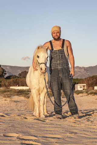 Spanien, Tarifa, lächelnder Mann mit Pony am Strand stehend, lizenzfreies Stockfoto