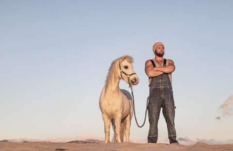 Spanien, Tarifa, Mann mit Pony am Strand stehend, lizenzfreies Stockfoto