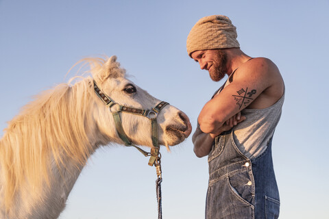 Lächelnder Mann vor Pony unter blauem Himmel, lizenzfreies Stockfoto