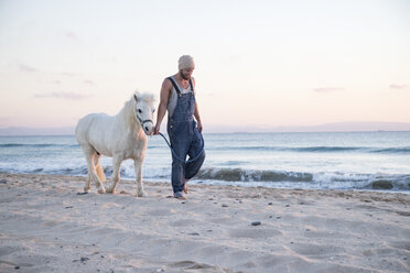 Spanien, Tarifa, Mann geht mit Pony am Strand spazieren - KBF00487
