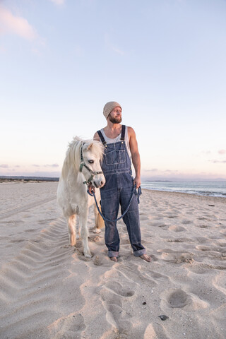 Spanien, Tarifa, Mann mit Pony am Strand stehend, lizenzfreies Stockfoto