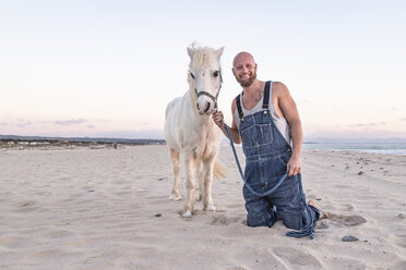 Spain, Tarifa, portait of smiling man with pony on the beach - KBF00490