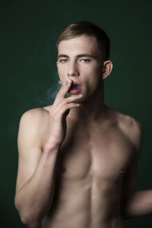 Porträt eines selbstbewussten nackten jungen Mannes, der im Studio eine Zigarette raucht - VWF00060
