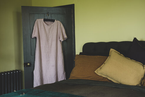 Innenansicht eines Schlafzimmers mit hellgrünen Wänden, einem Doppelbett und einem blassrosa Leinennachthemd auf einem Kleiderbügel über der Tür. - MINF10183