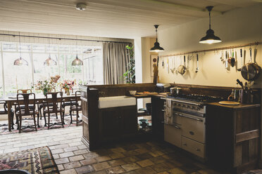 Innenansicht der Küche mit Steinfliesenboden, Herd und Butler-Spüle, offen zum Wintergarten mit antikem Holztisch und Stühlen. - MINF10192