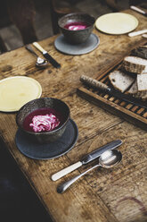 Nahaufnahme von schwarzen Schüsseln mit Rote-Bete-Suppe und Brot auf einem alten Holztisch. - MINF10206