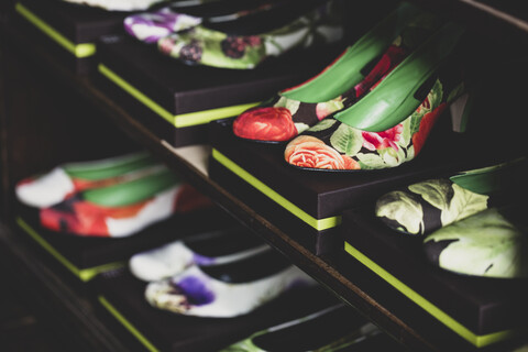 Nahaufnahme von hochhackigen Schuhen mit bunten Blumenmustern auf braunen Kisten, die auf Holzregalen aufgereiht sind., lizenzfreies Stockfoto