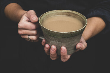 High angle close up of human hands holding green earthenware mug of tea. - MINF10303
