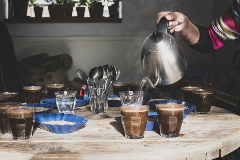 Kaffeeverkostung, Barista gießt Kaffee in Gläser auf einem Holztisch, Tabletts mit Kaffeebohnen. - MINF10319