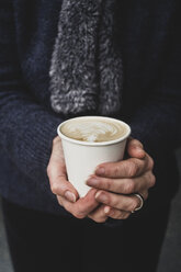 Nahaufnahme einer Person, die einen Pappbecher mit Cafe Latte hält, der mit einem komplizierten Schaummuster bedeckt ist. - MINF10332