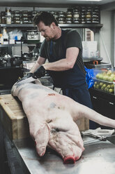 Männlicher Metzger mit Schürze und schwarzen Gummihandschuhen, der einen Schweineschlachtkörper auf einem Fleischerblock zerlegt. - MINF10364