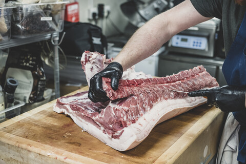 Nahaufnahme eines Metzgers mit schwarzen Gummihandschuhen, der Schweinerippchen auf einem Fleischerblock schneidet., lizenzfreies Stockfoto