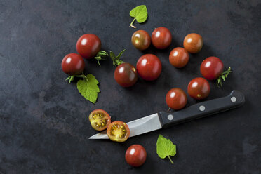 Whole and sliced risp tomatoes 'Black Cherry', leaves and kitchen knife on dark ground - CSF29216