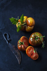 Ganze und in Scheiben geschnittene Rindertomaten 'Chocolate Stripes' und Messer auf dunklem Grund - CSF29237