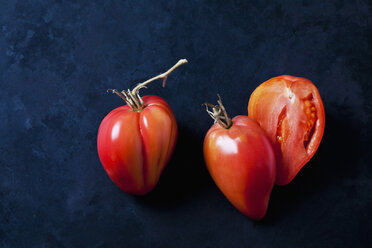 Ganze und in Scheiben geschnittene Ochsenherz-Tomaten auf dunklem Grund - CSF29278